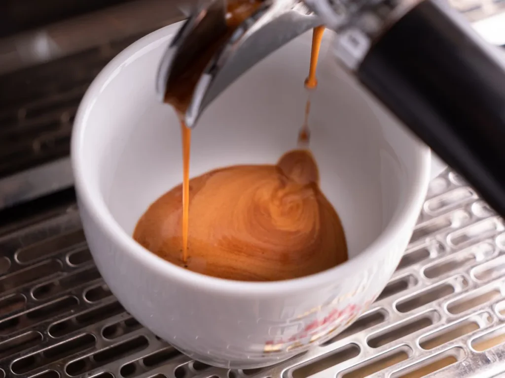 Espresso pouring from a machine into a white cup.