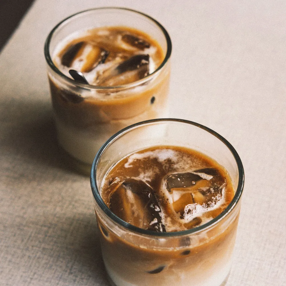 Two glasses of iced coffee with layers of milk and ice on a table.
