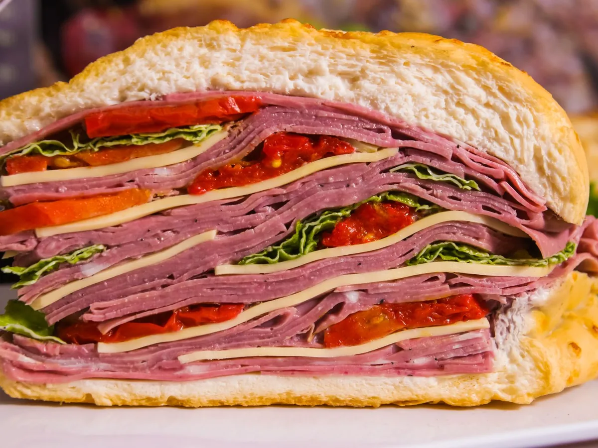 A cross-section of a layered sandwich with cured meat, cheese, lettuce, and tomato.