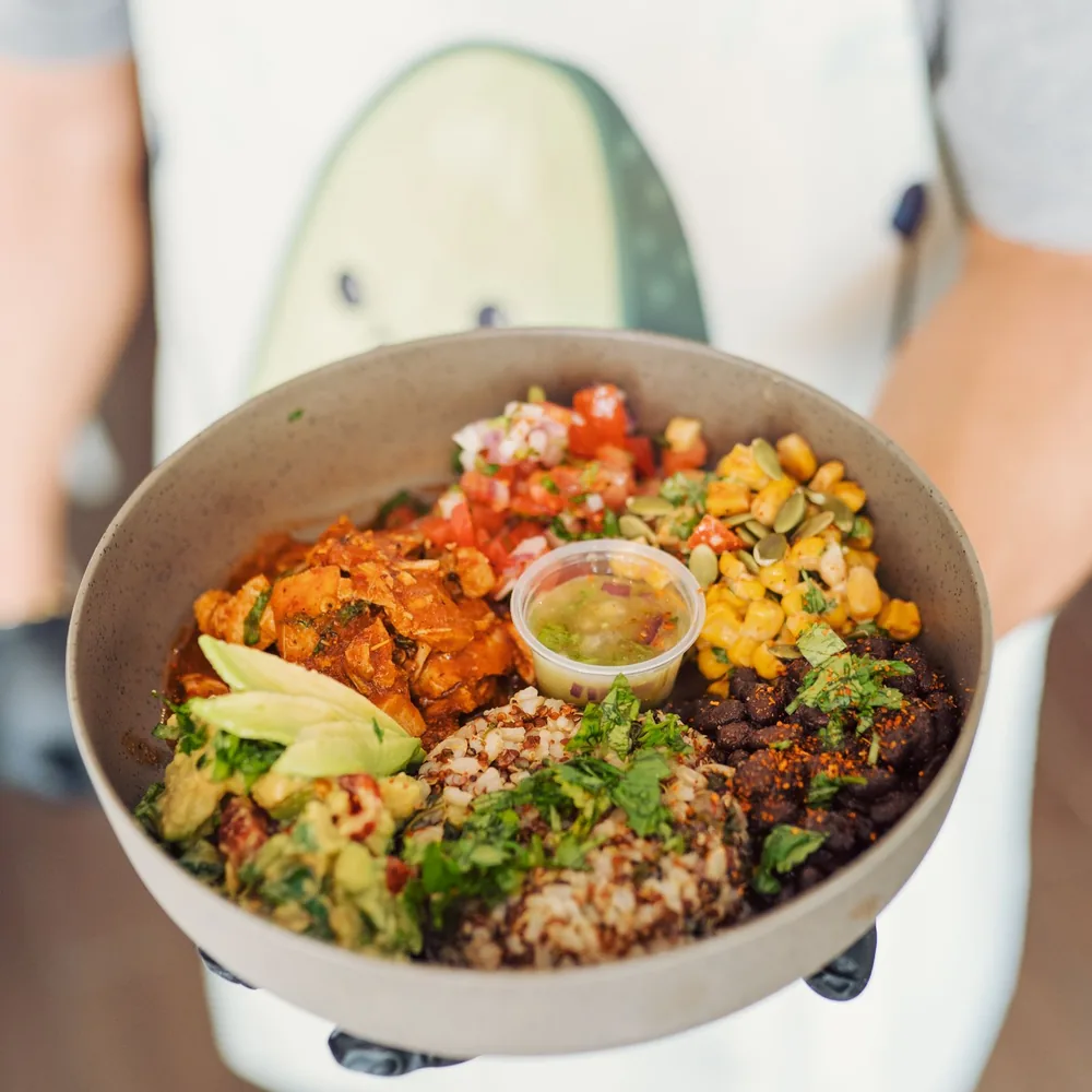 A person holding a bowl of rice, beans, sweetcorn, salsa, and sliced avocado.
