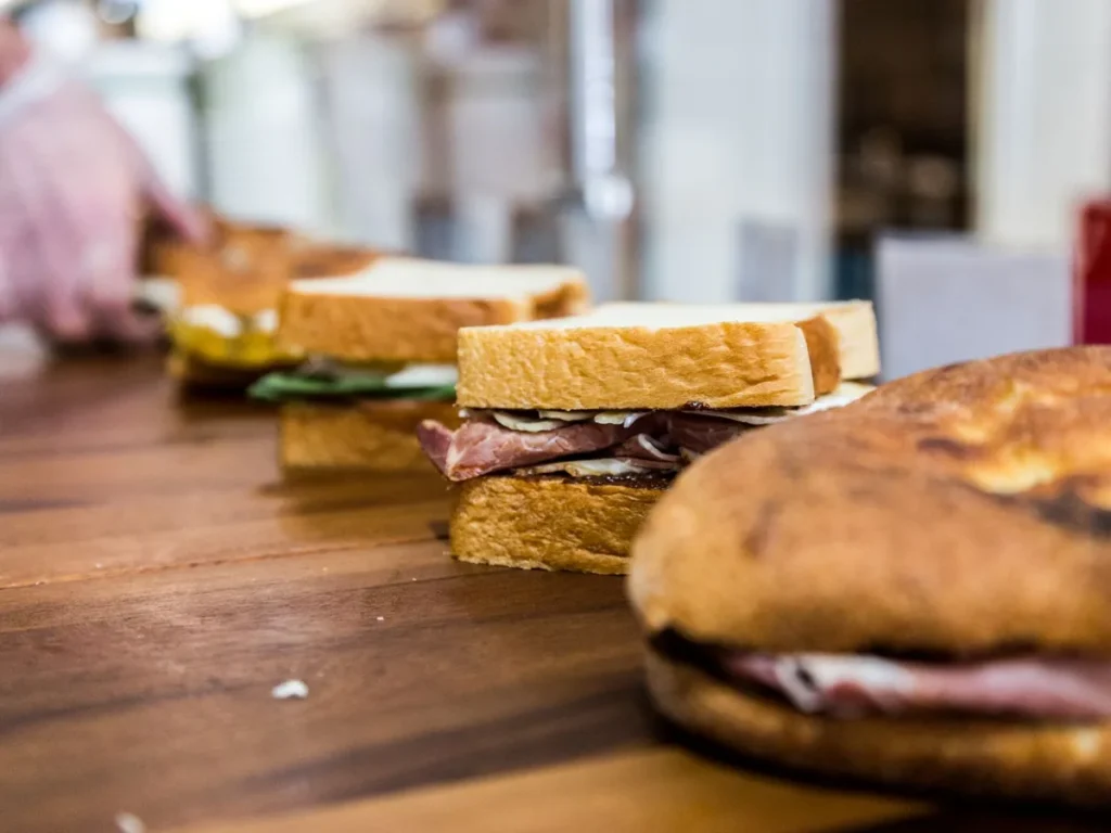 A row of filled sandwiches with sliced meat and cheese on a wooden counter.