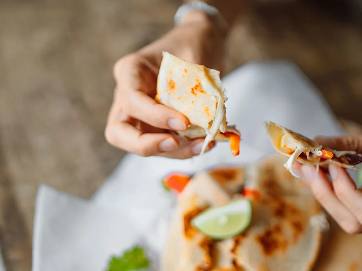 Hands pulling apart a folded tortilla with melted cheese stretching between the halves.