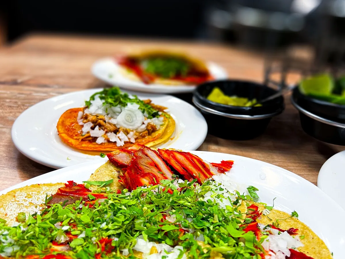 Plates of soft tacos topped with sliced meat, diced onion, and cilantro beside bowls of lime wedges.
