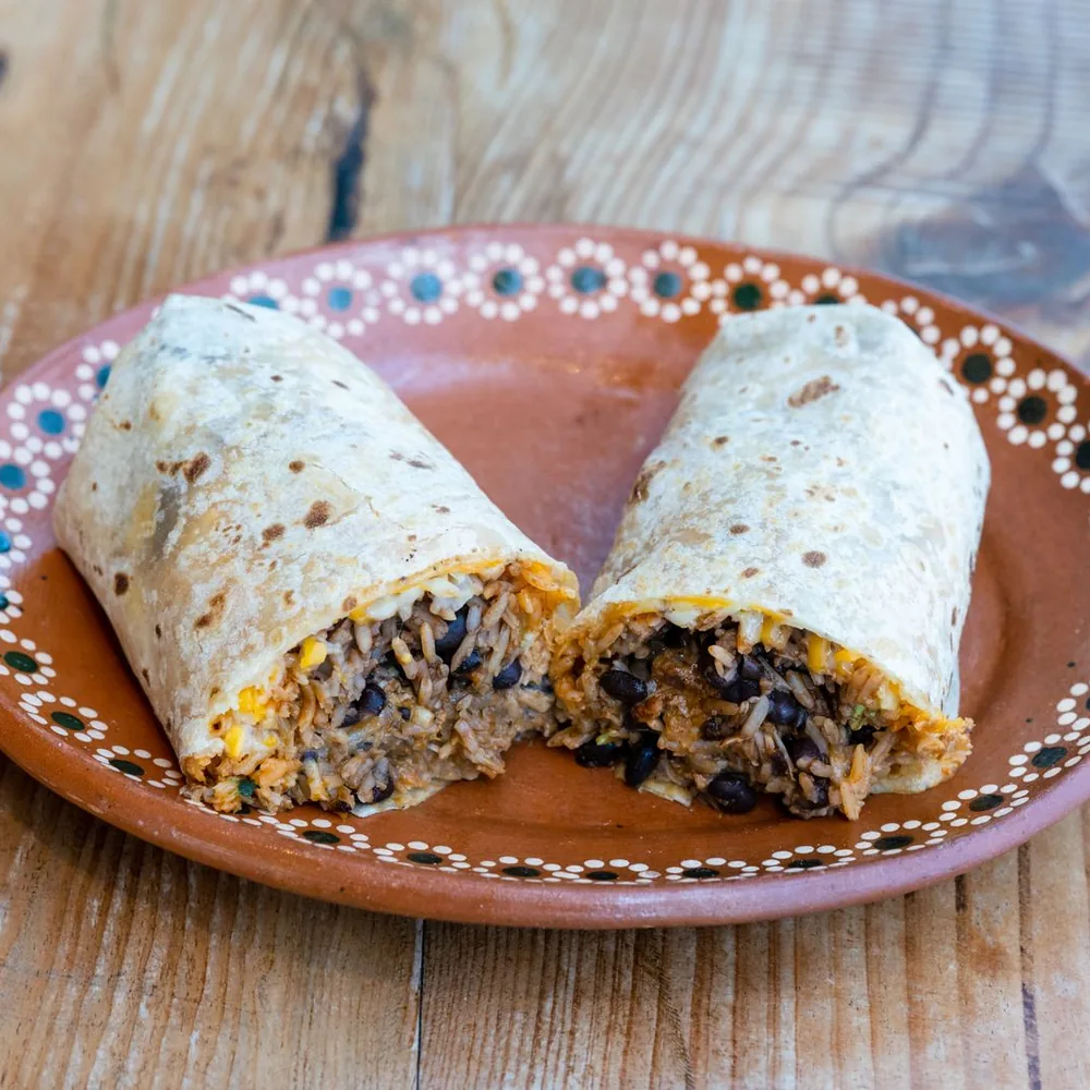A burrito cut in half showing rice, black beans, and meat on a patterned plate.