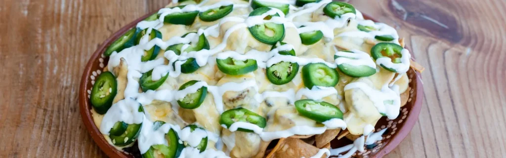 Nachos topped with melted cheese, a drizzle of sour cream, and sliced jalapeños.