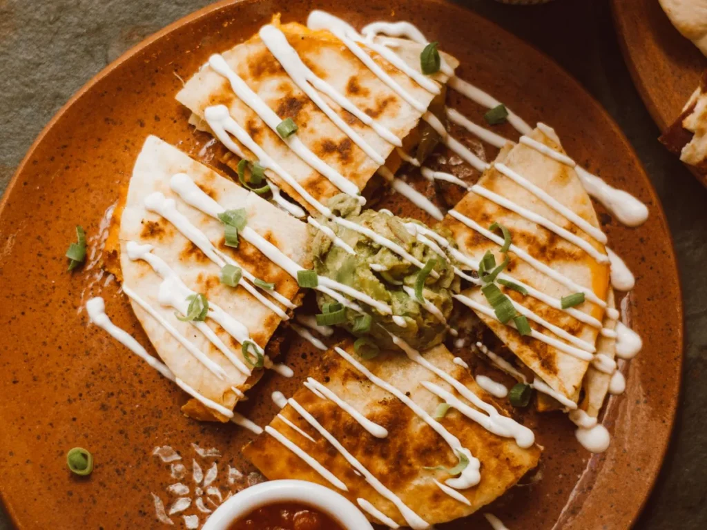 Grilled quesadilla wedges drizzled with sauce and served with guacamole and salsa.
