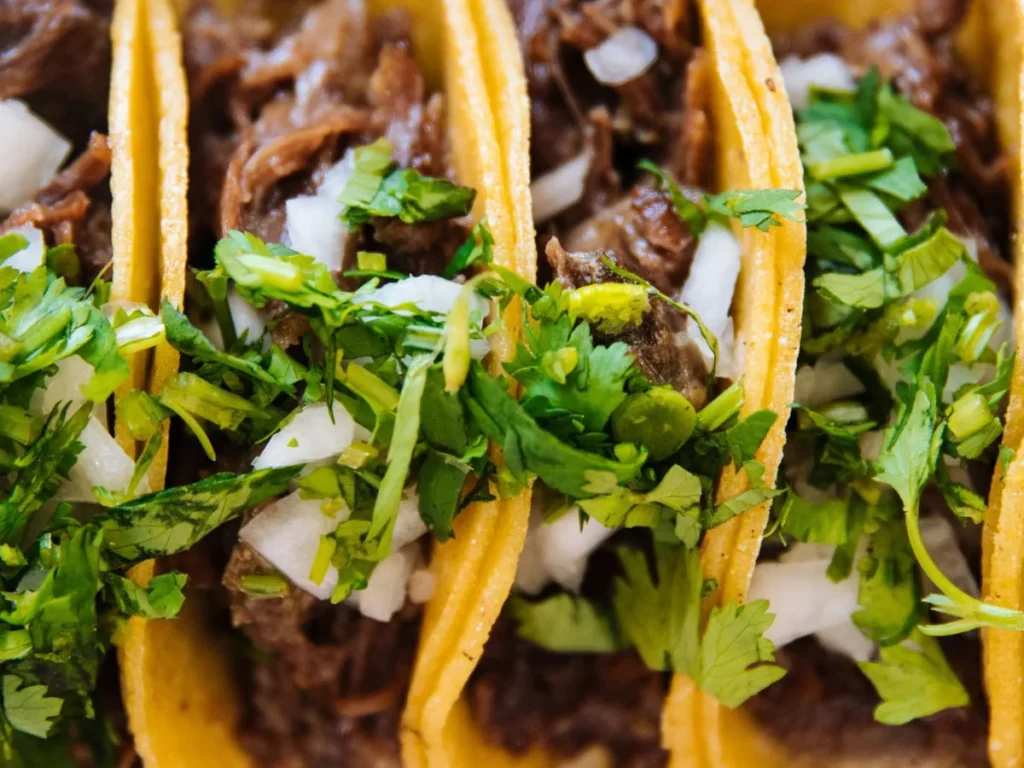 Close-up of hard-shell tacos filled with shredded meat, diced onion, and fresh cilantro.