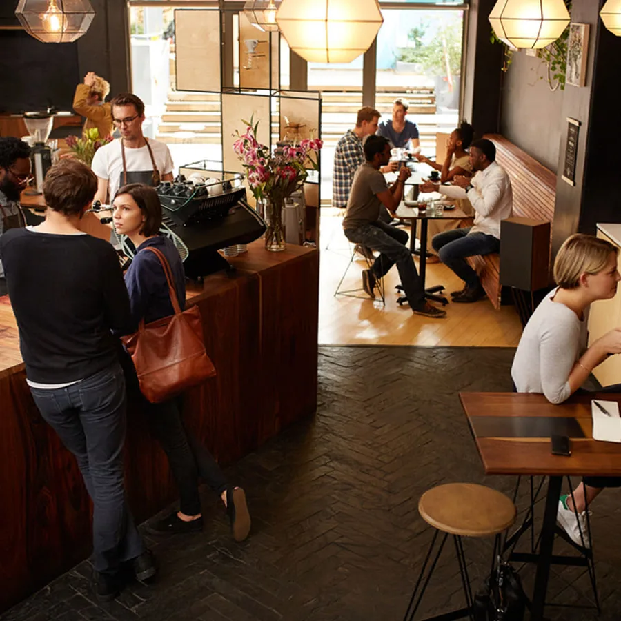 Customers ordering at a cafe counter and sitting at tables inside a busy cafe.