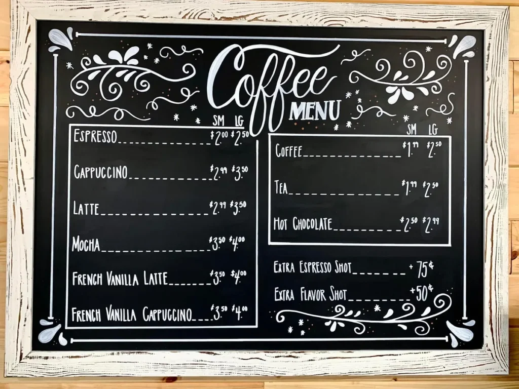 A framed chalkboard coffee menu listing espresso, cappuccino, latte, tea and hot chocolate with prices.