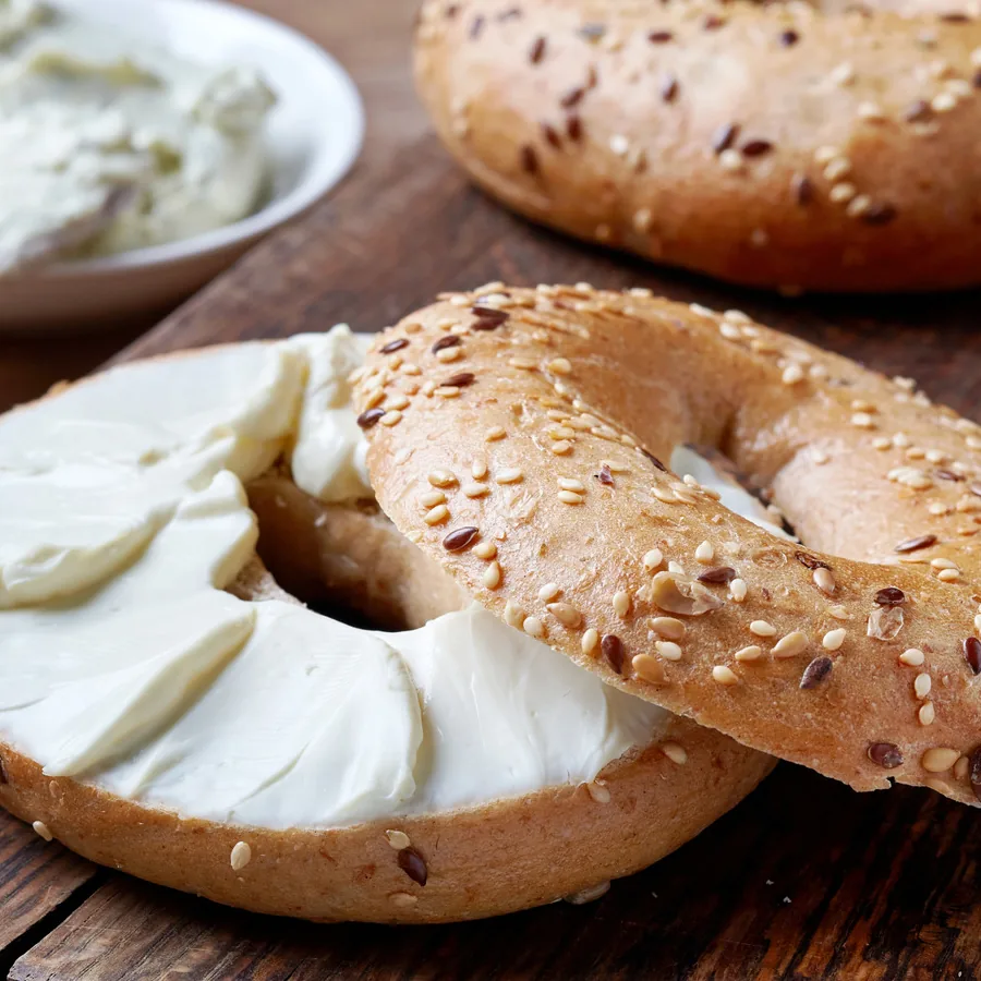 Seeded bagel halves spread with cream cheese on a wooden board.