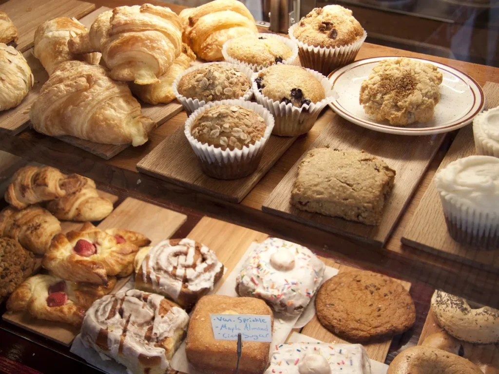 A bakery display of croissants, muffins, cinnamon rolls and cookies on wooden boards.