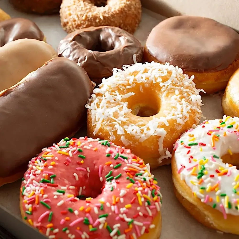 Assorted donuts with chocolate glaze, coconut, pink frosting and sprinkles in a box.