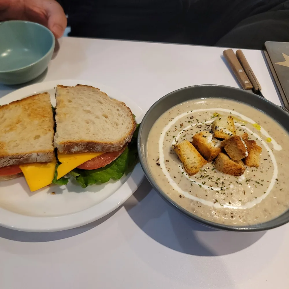 A toasted cheese and tomato sandwich beside a bowl of creamy soup topped with croutons.