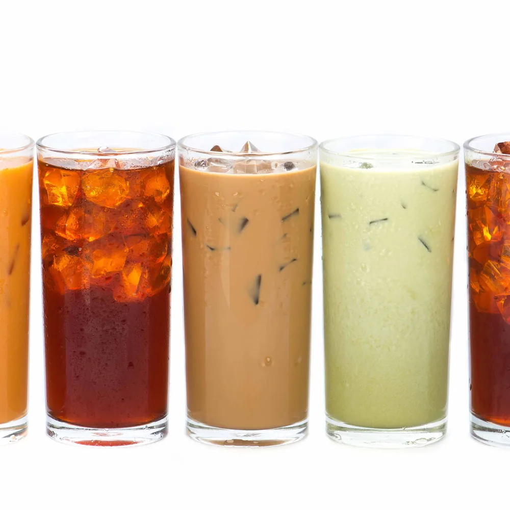 A row of tall glasses of iced tea, iced coffee and a pale green iced drink.