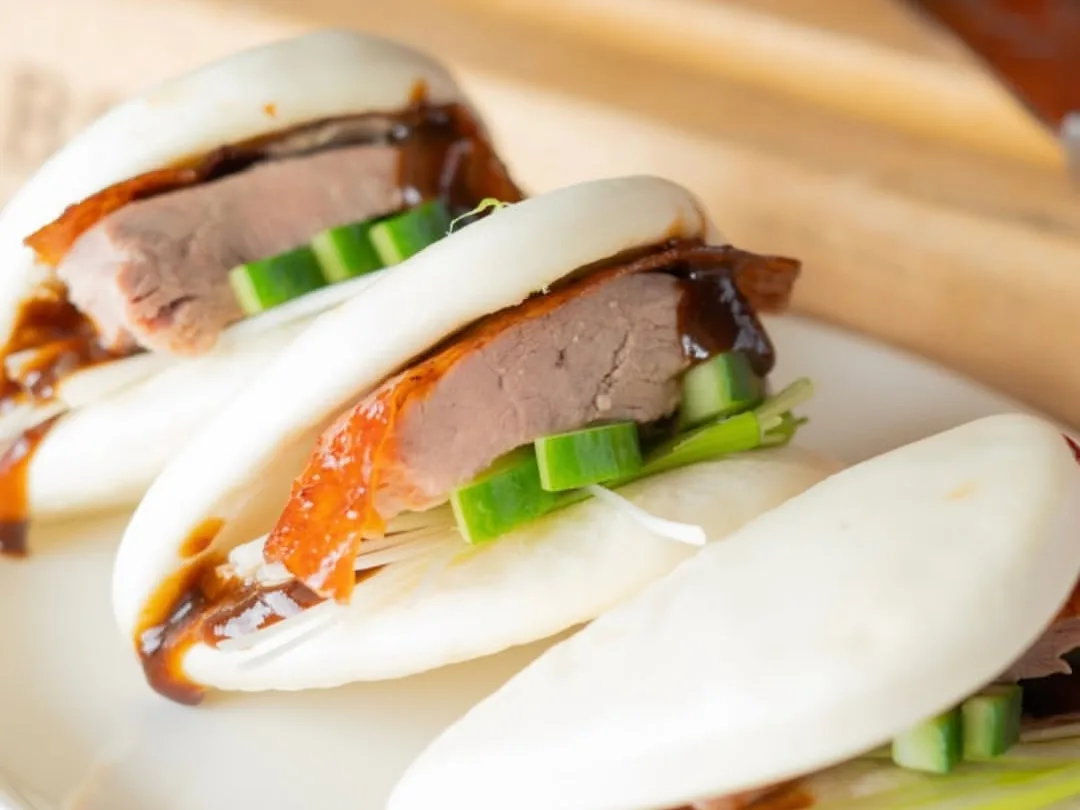 Two steamed buns filled with sliced meat, cucumber, and spring onion on a plate.
