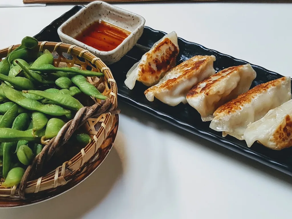 Pan-fried gyoza dumplings and a basket of edamame with a small bowl of dipping sauce.